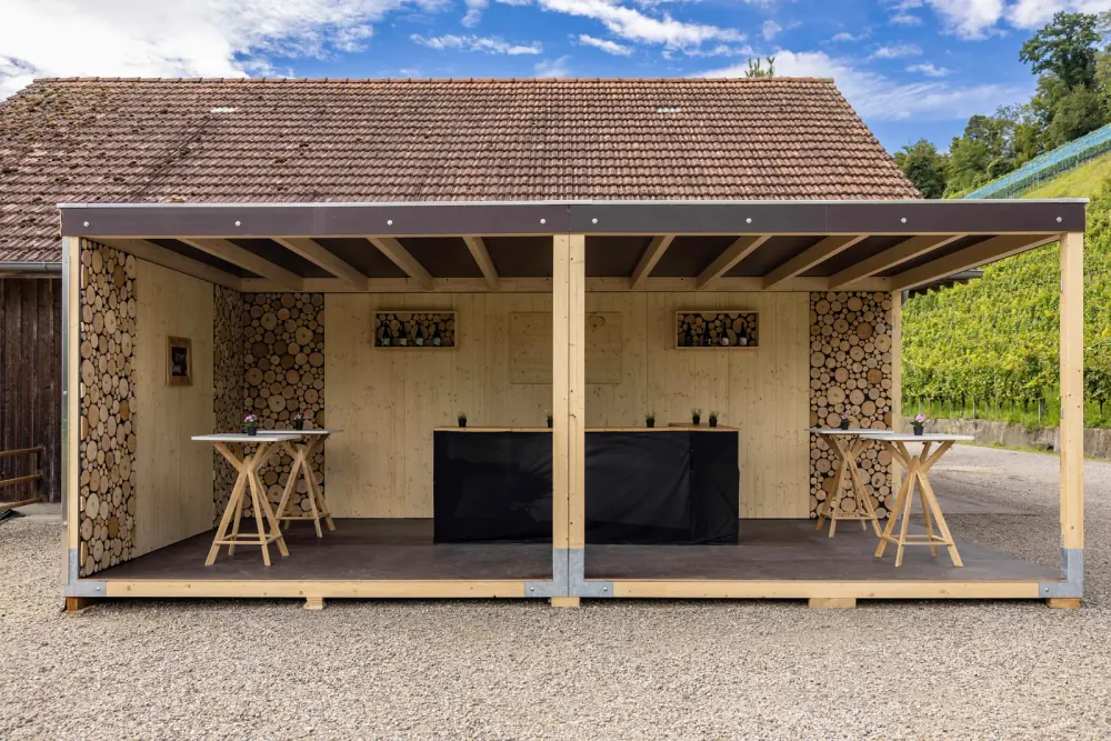 Modul Chalet mit Brennholzwänden vor der Scheune